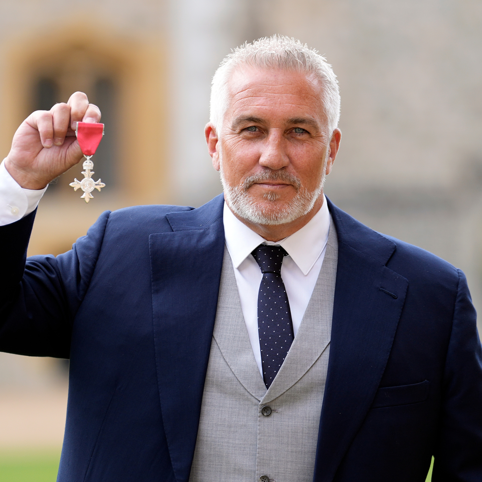  Paul Hollywood in navy suit after being made a Member of the Order of the British Empire. He is hold up his medal.