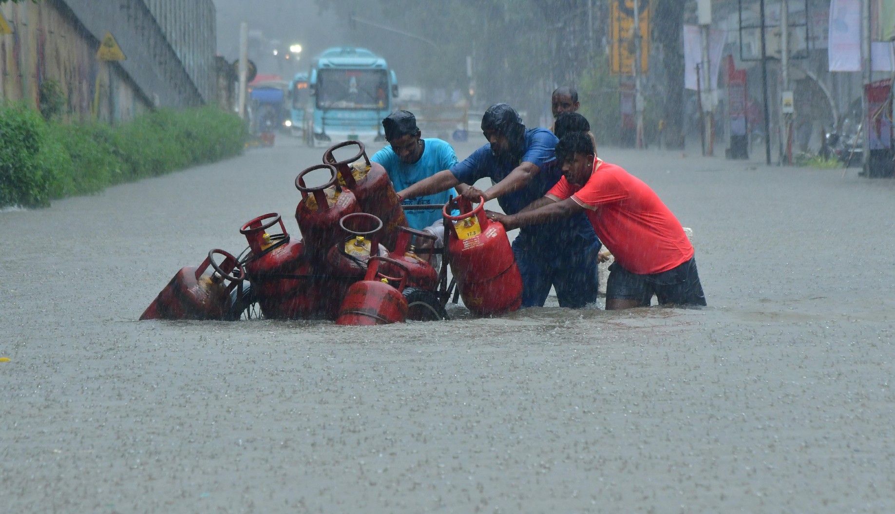 Men pushing a cart of gas canisters through thigh-high water on a flooded street in Mumbai during a downpour