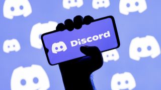 Smartphone with the Discord social gaming platform logo on the screen in a clenched hand on the background of Discord logos
