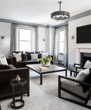 Black and gray modern living room with gray painted ceiling trim, gray curtains, two black sofas, large square coffee table and black armchair, rounded metal pendant light and matching side table, seating area centered around fire place
