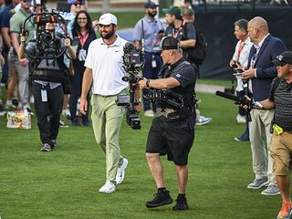 Scottie Scheffler being followed by television camera operators on a golf course