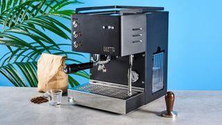 The Diletta Mio espresso machine on a stone surface with a bag of coffee beans and a tamp