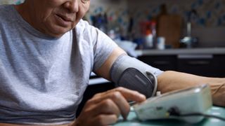 Man sitting at a table using a blood pressure monitor