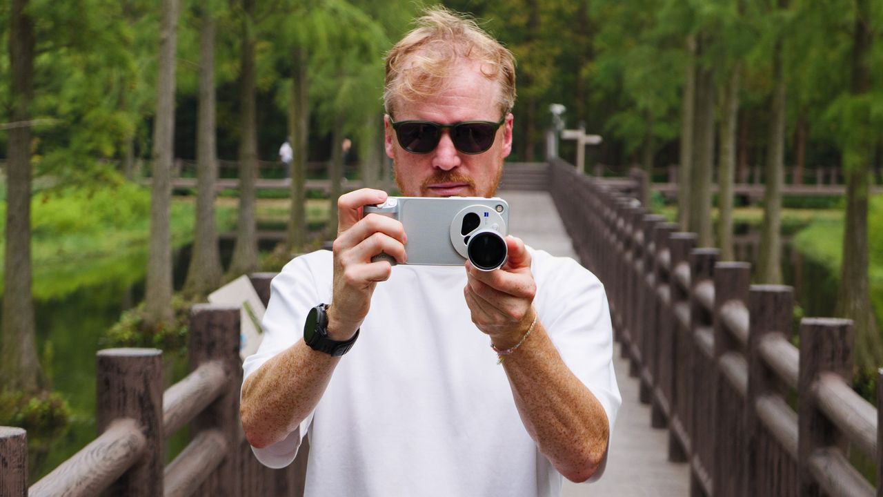 Tim Coleman, TechRadar's Cameras Editor, holding the Vivo X500 Pro Max phone with teleconverter lens attached, while stood on a wooden walkway in a birdlife reserve in Shanghai, China