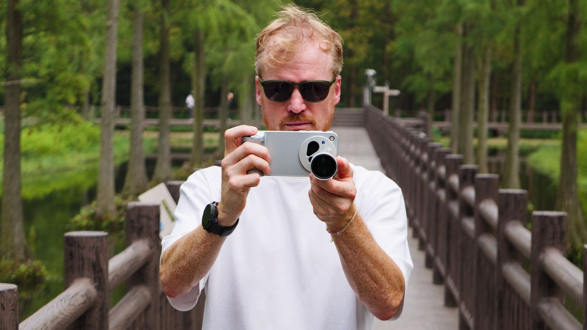 Tim Coleman, TechRadar's Cameras Editor, holding the Vivo X500 Pro Max phone with teleconverter lens attached, while stood on a wooden walkway in a birdlife reserve in Shanghai, China