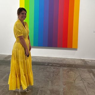 Princess Eugenie standing in front of a rainbow painting wearing a yellow maxi dress and sneakers