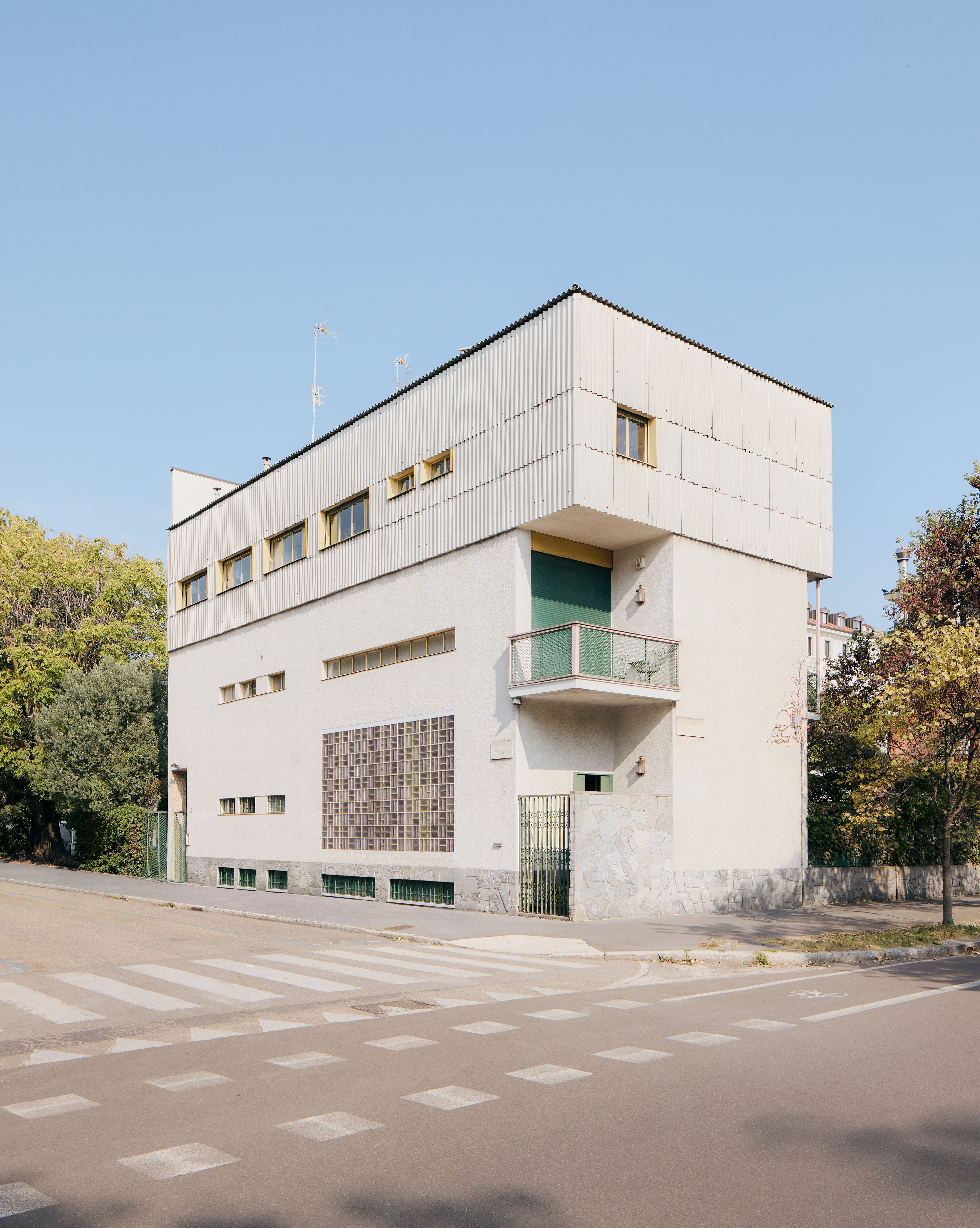 A sun-lit view of a modernist villa with a geometric, rectangular silhouette, checkered motifs, small windows, and a green-on-white palette.