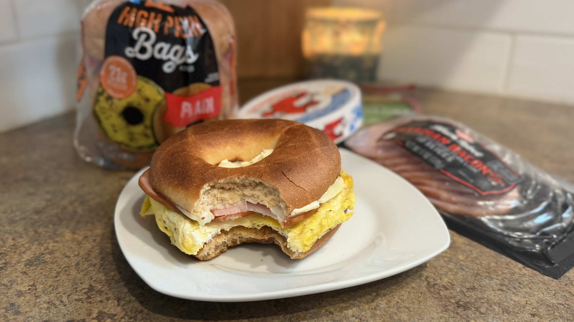 Bagel with a bite taken out of it on a plate with packets of ingredients in background