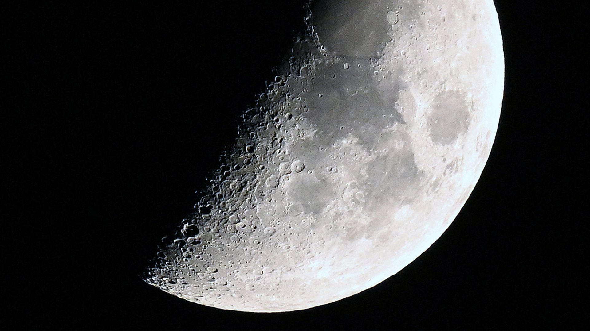 A photo of the moon with its right side lit around the first quarter phase in a black sky.
