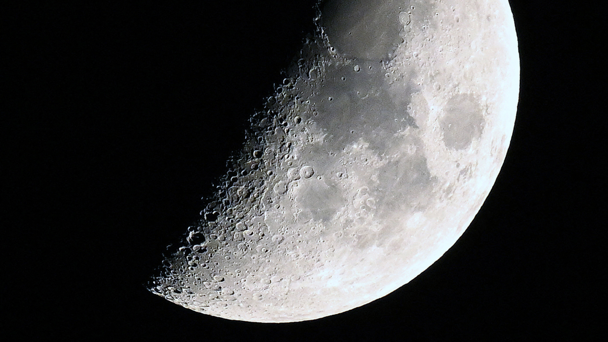 A photo of the moon with its right side lit around the first quarter phase in a black sky.