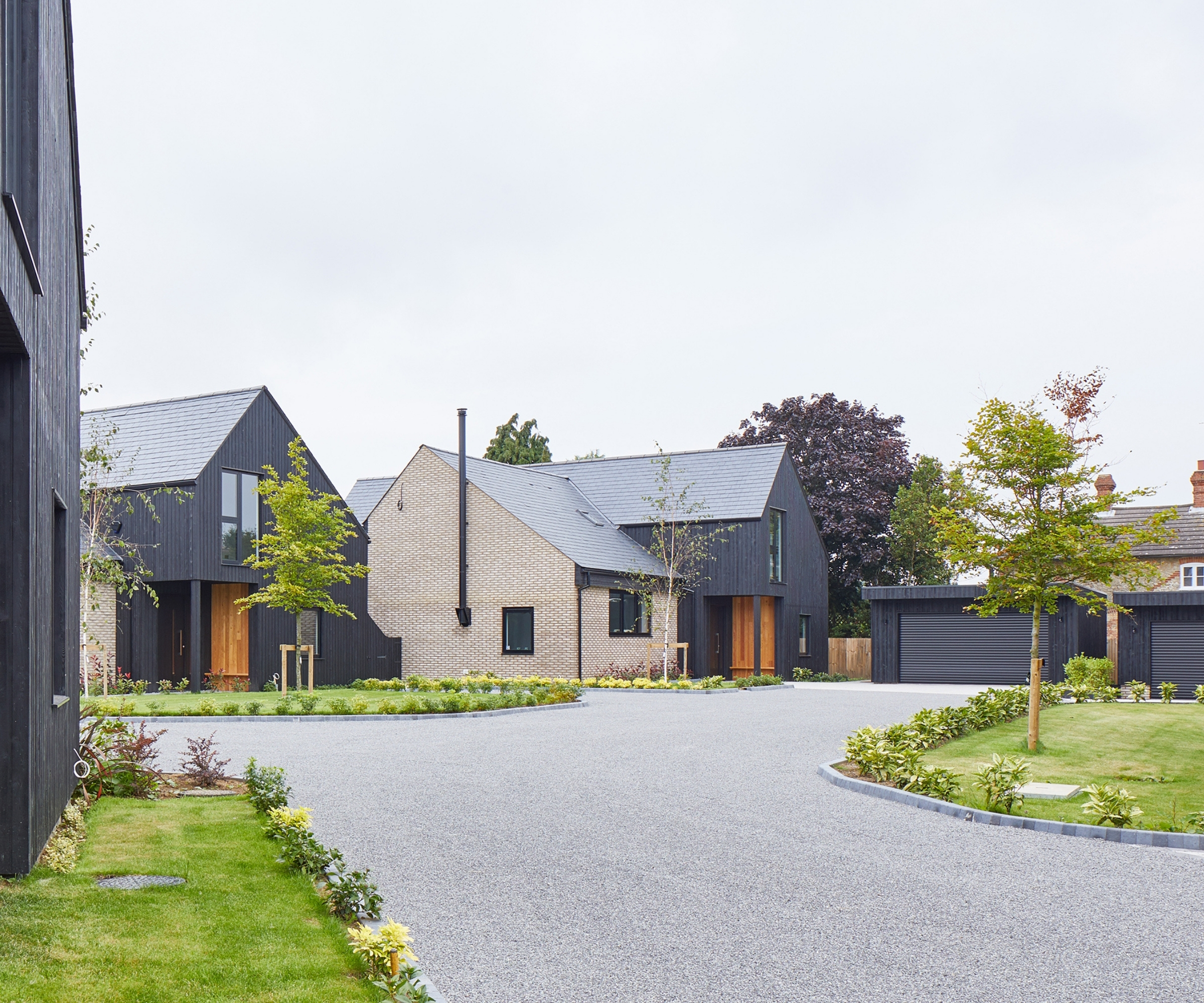 Modern black-timber and brick houses with a curved gravel driveway edged in stone, lawns, and young trees.
