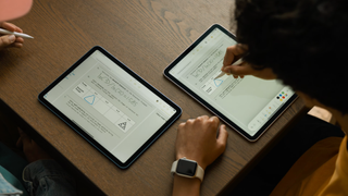 A top-down shot of two iPads on a table, each with its own user, with the user on the right drawing a triangle on a PDF on which the two are collaborating and the same triangle appearing in real-time on the PDF displayed on the left user's iPad.