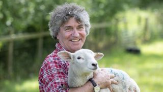 Martin Hughes-Games outdoors in a red checked shirt holding a lamb for Summer on the Farm
