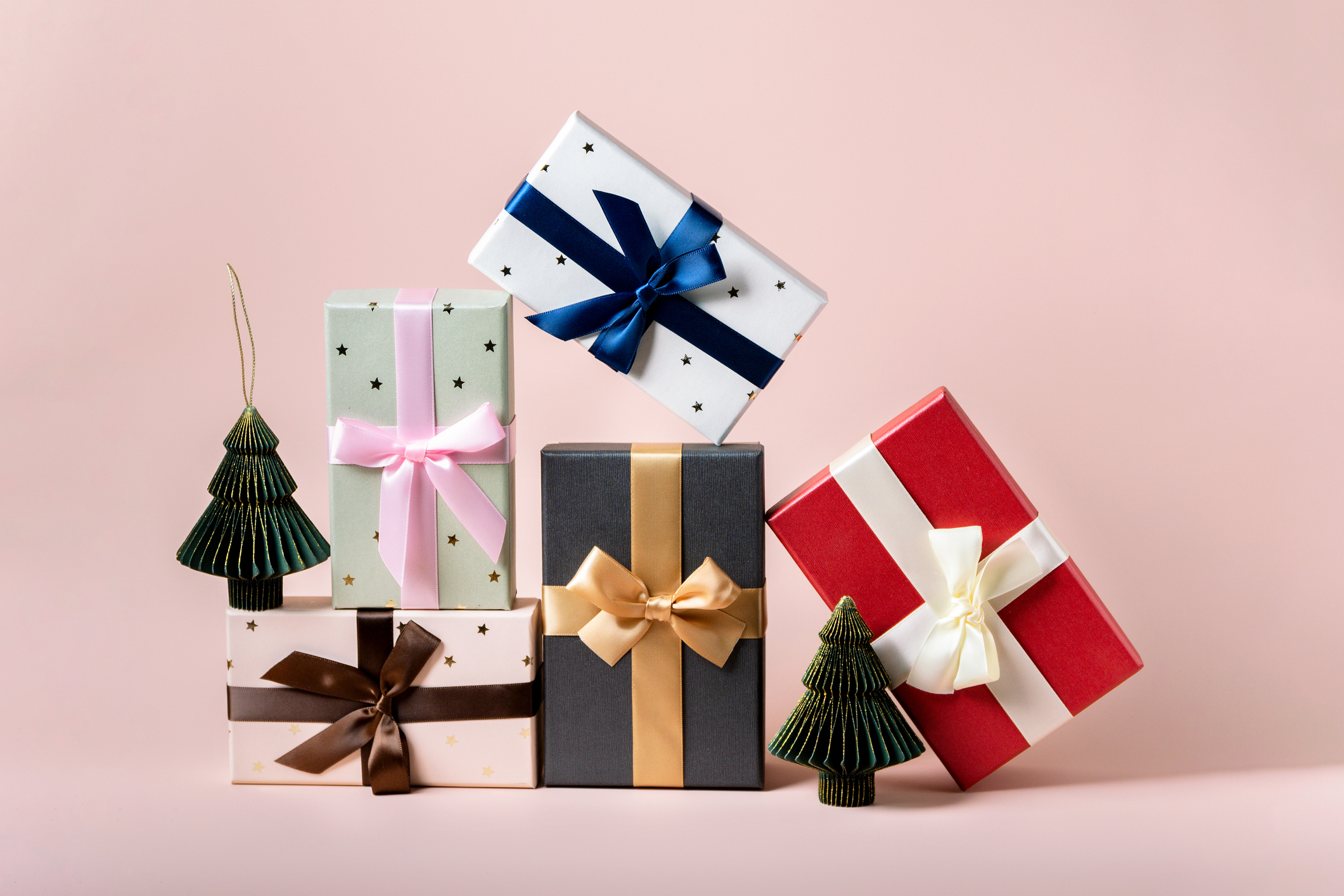 Light pink background with festive colourful Christmas presents in various colours with bows.