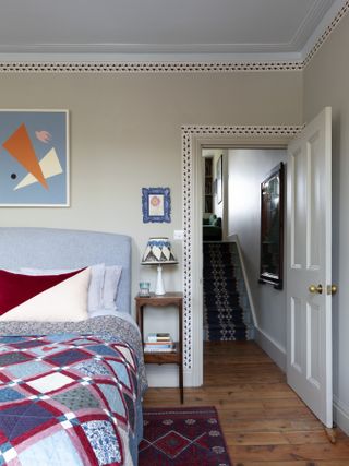 An eclectic bedroom with wooden flooring, a red patterned rug, and a patterned wallpaper border around beige wallls