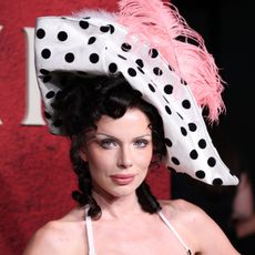 a white woman with dark hair wearing a white hat with black polka dots and a pink feature