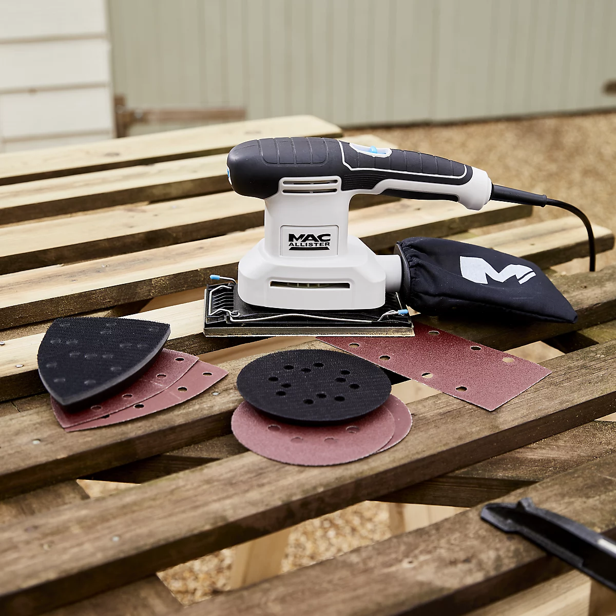 mac allister 200w corded multi-sander sat on a wooden pallet with 3 x sanding pads and sandpaper