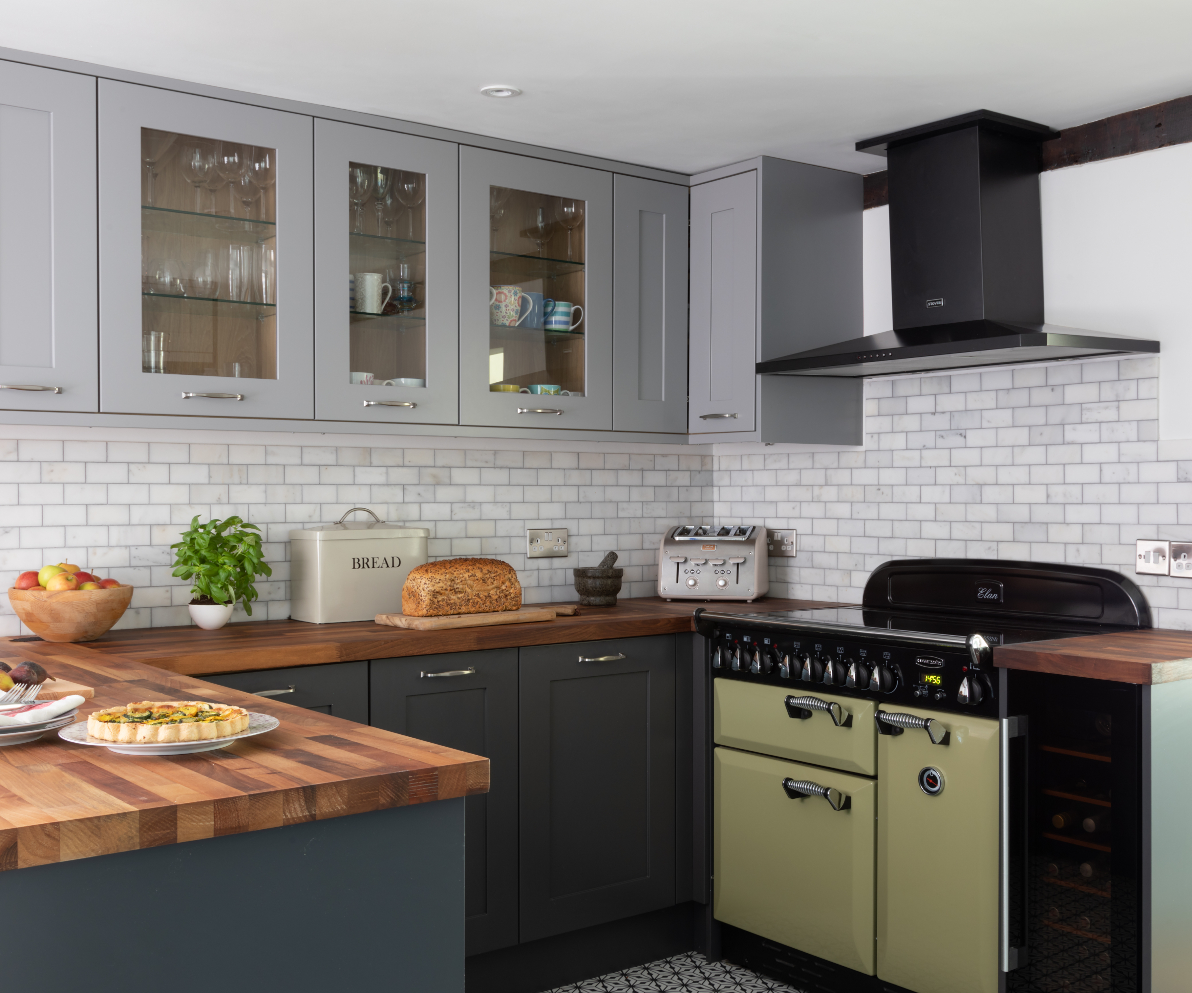 kitchen with grey wall cabinets with glass fronts, darker grey base units, wooden worktop and white metro tiles