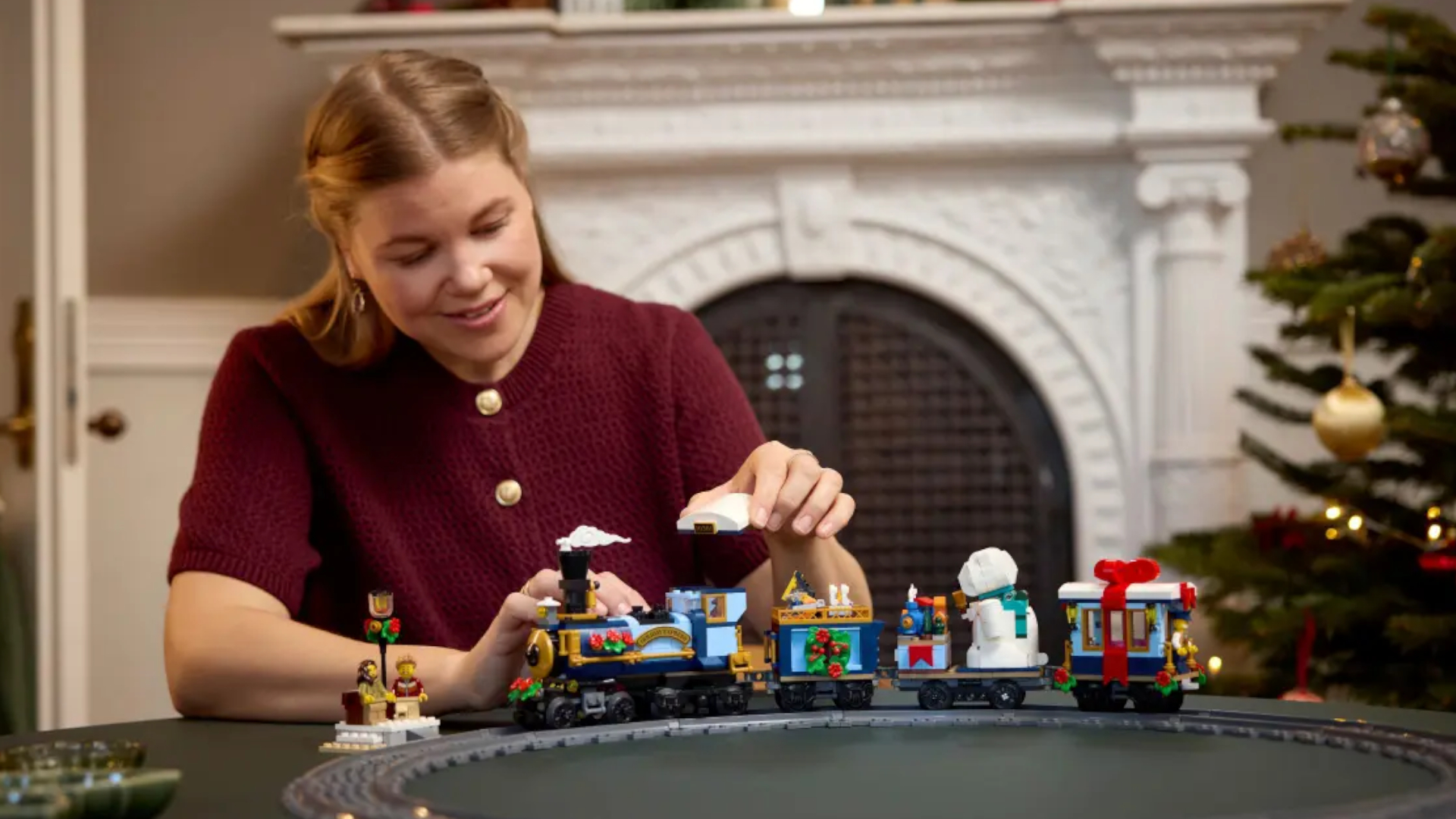 A woman smiles while placing the top on the steam engine in the Holiday Express Train set