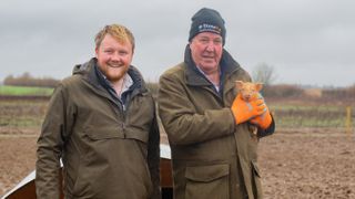 Kaleb Cooper with Jeremy Clarkson holding a brown piglet for Clarkson's Farm season 3