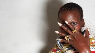 Black woman holding up her hand with microchipped manicure and gold rings