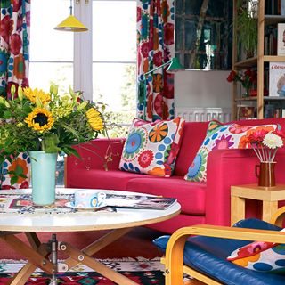A retro living room with a red sofa and colourful pattered curtains and cushions