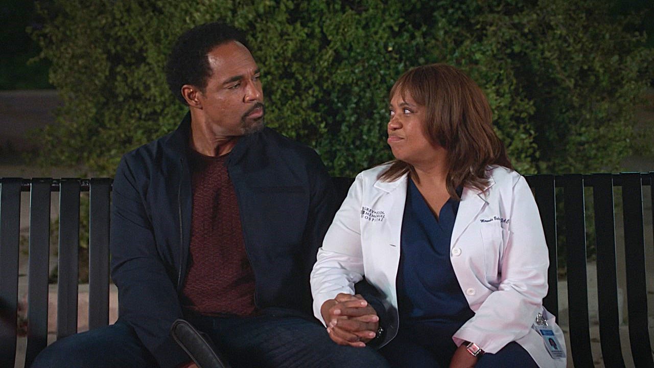 Ben Warren (Jason George) and Miranda Bailey (Chandra Wilson) hold hands and look at each other while sitting on a bench outside the hospital on Grey's Anatomy's Season 21 finale.