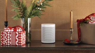 The Sonos One smart speaker in white pictured on a cabinet surrounded by presents and candles