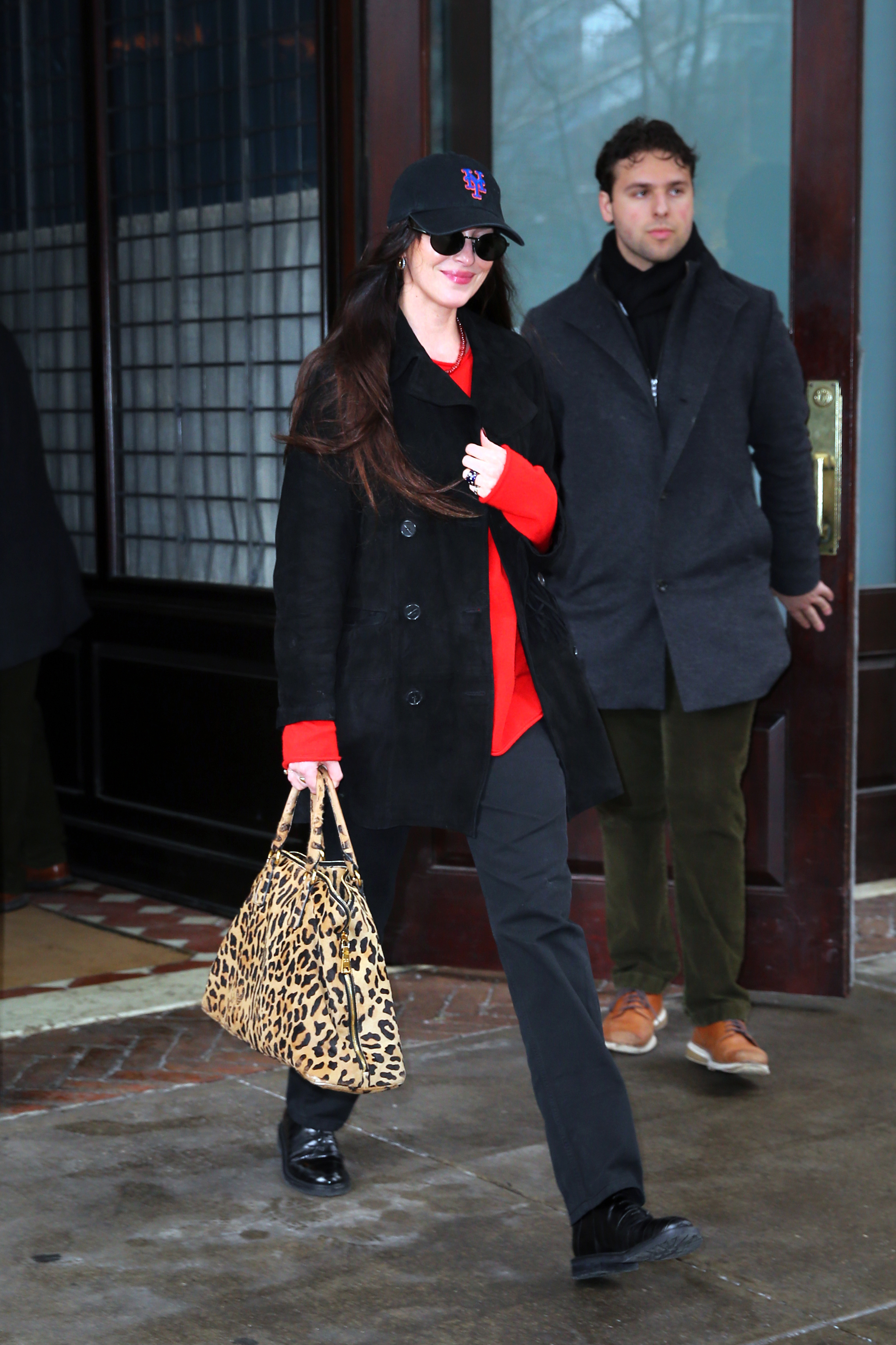 Dakota Johnson was spotted in New York City wearing a black pea coat, a red sweater, a suede jacket, leather boots, and a leopard-print Prada bag