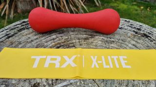 Image shows a yellow TRX Strength Band next to a red weight.