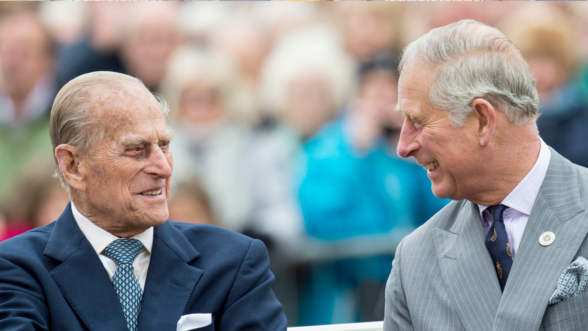 Prince Philip wearing a blue suit smiling at Prince Charles