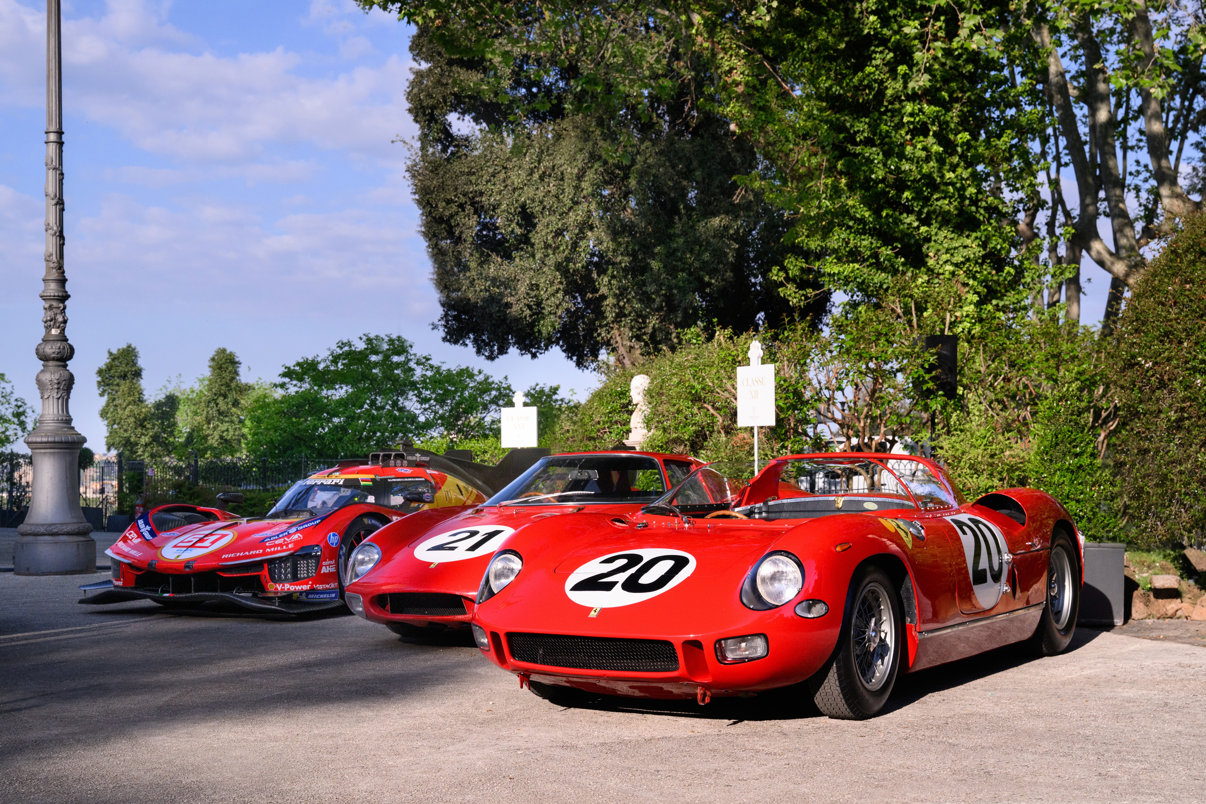 Three Ferrari competition cars are displayed at Anantara Concorso Roma, led by a red Ferrari 250 LM, with historic and modern racing machines lined up beneath the trees.
