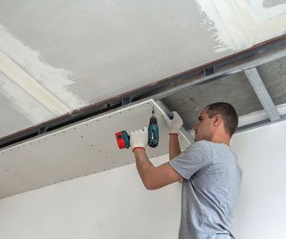 male installing suspended ceiling frame and plasterboard on top