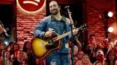 Noah Kahan performing on stage with a guitar