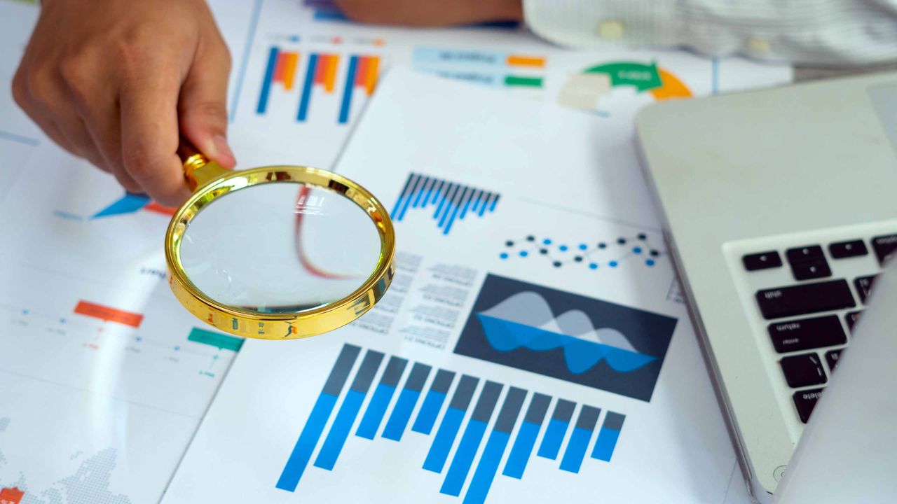 Person looking at financial charts with magnifying glass