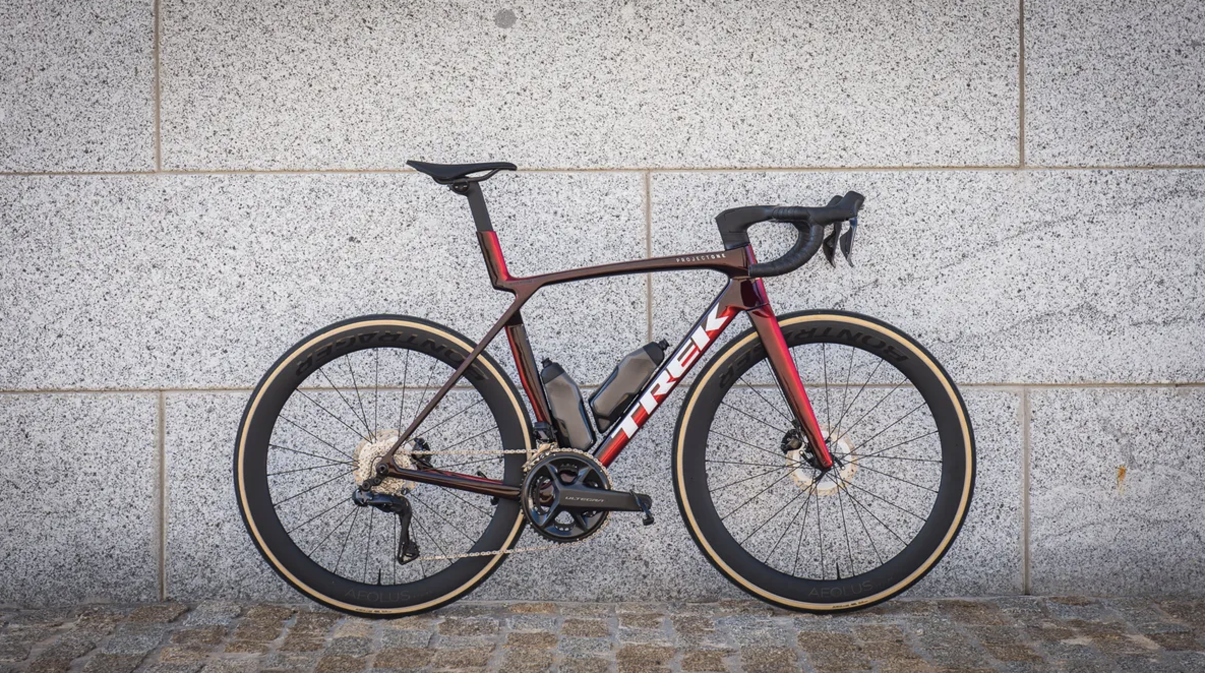 A red Trek lightweight bike sits in front of a grey concrete block wall