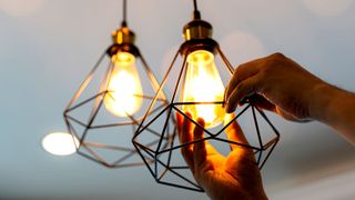 Hands installing a decorative antique edison style filament light bulb into a wire frame light shade against a white ceiling