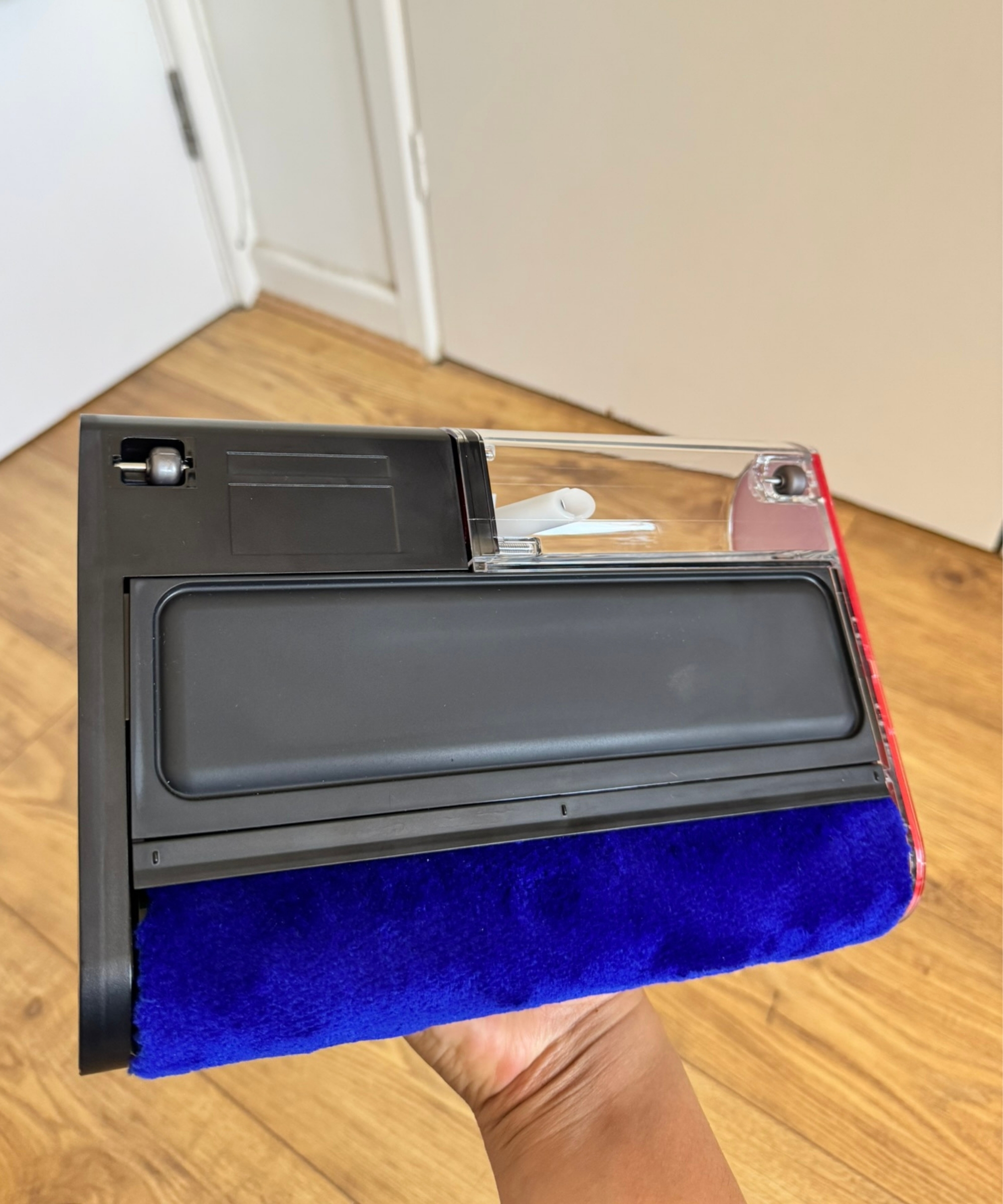 Hand holding the Dyson PencilWash floorhead above wooden floor and white doors.