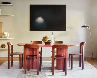 Orange lacquer modern dining table with lacquer dining chairs in front of large dark artwork