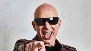 Joe Satriani in sunglasses, pointing at the camera