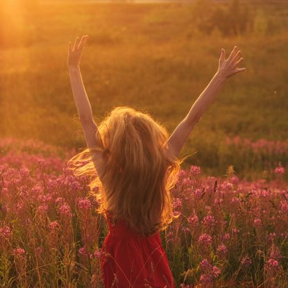 Woman dancing and jumping around in a field full of pink flowers 