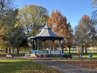 A photo of a bandstand in a park on a sunny day with trees and a blue sky in the background