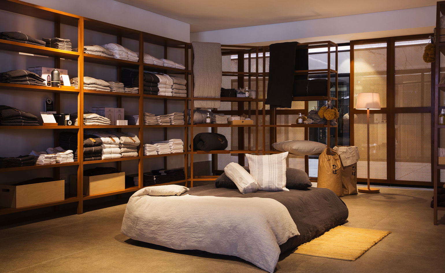 Double bed on the floor with white throw and shelves around the side with towels on