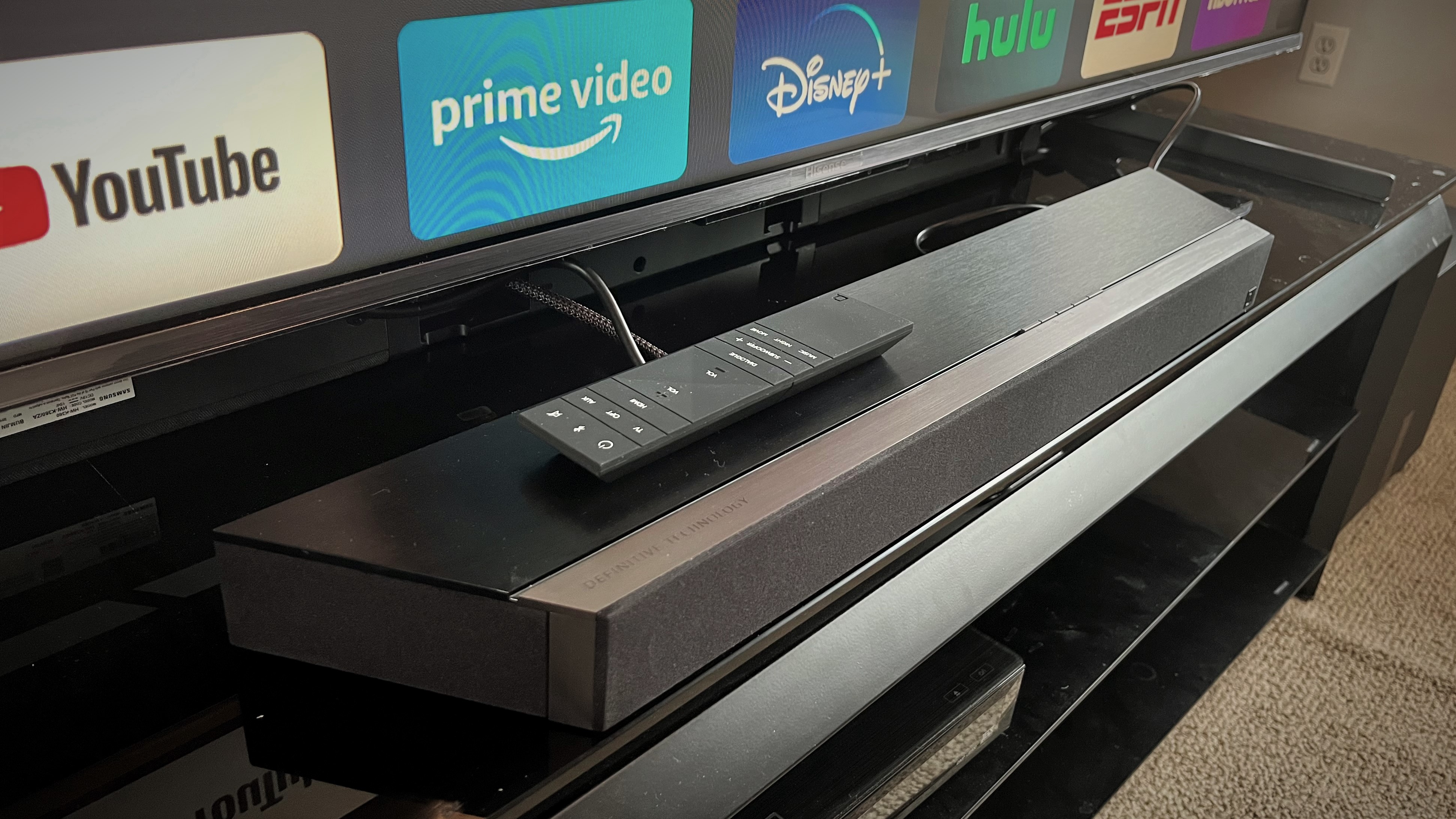 Definitive Technology Studio 3D Mini soundbar on TV stand with TV in background