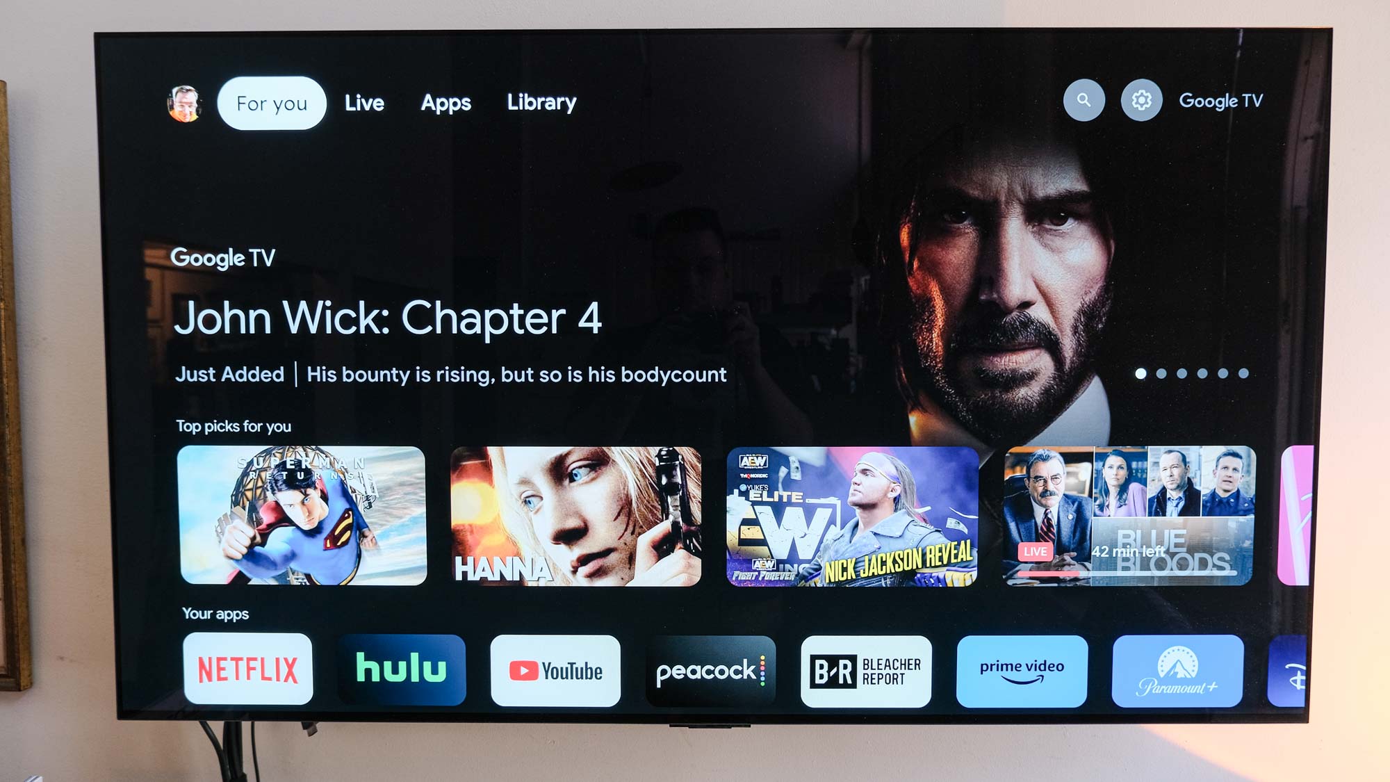 The TV is showing a promo for John Wick on the Google TV home screen coming from the Google TV 4K webcast box
