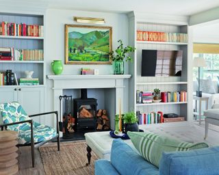 colorful living room with woodburner, paneled bookcases, patterned chair, blue sofa, white chair, stool and colorful patterned cushions