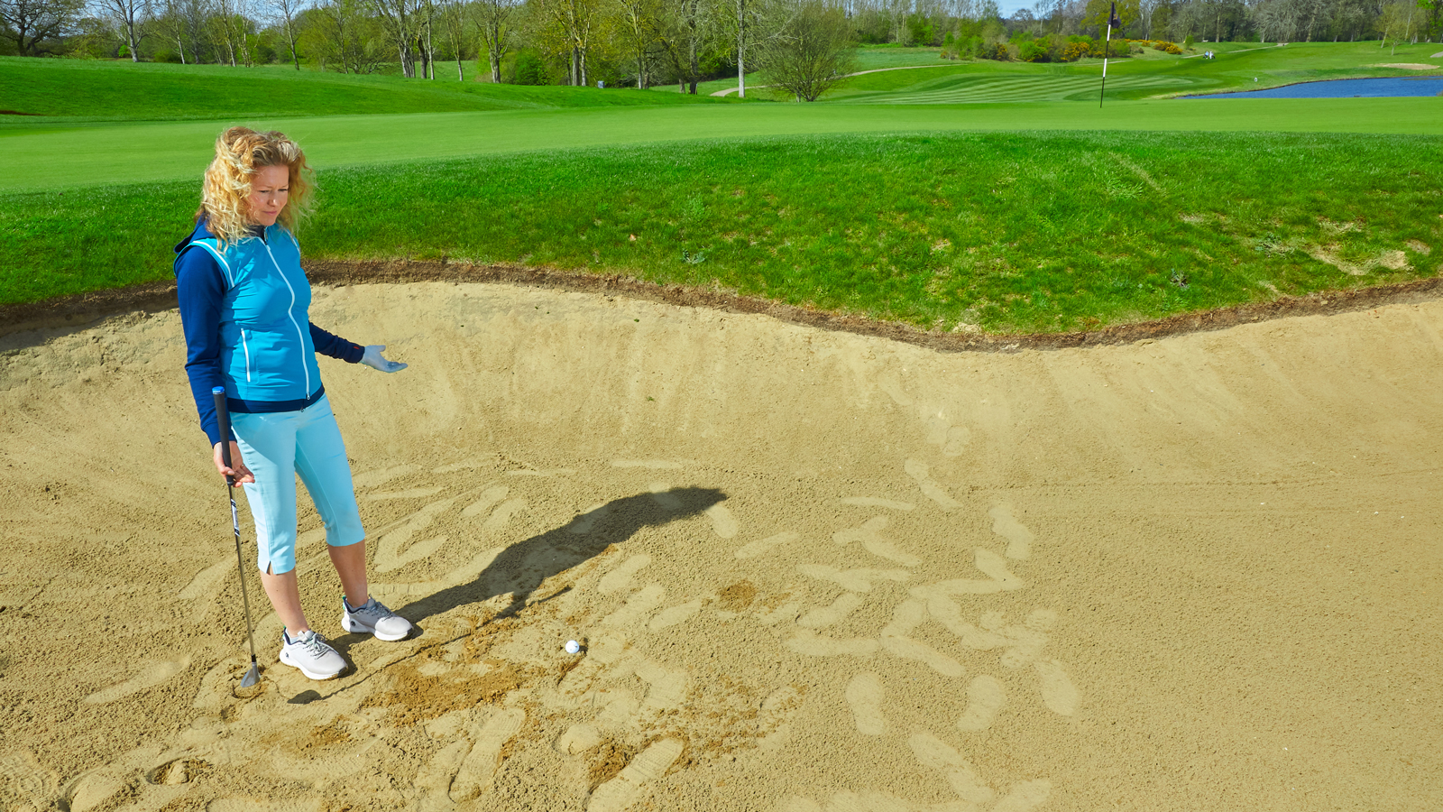 A golfer reacts to her golf ball in an unraked bunker