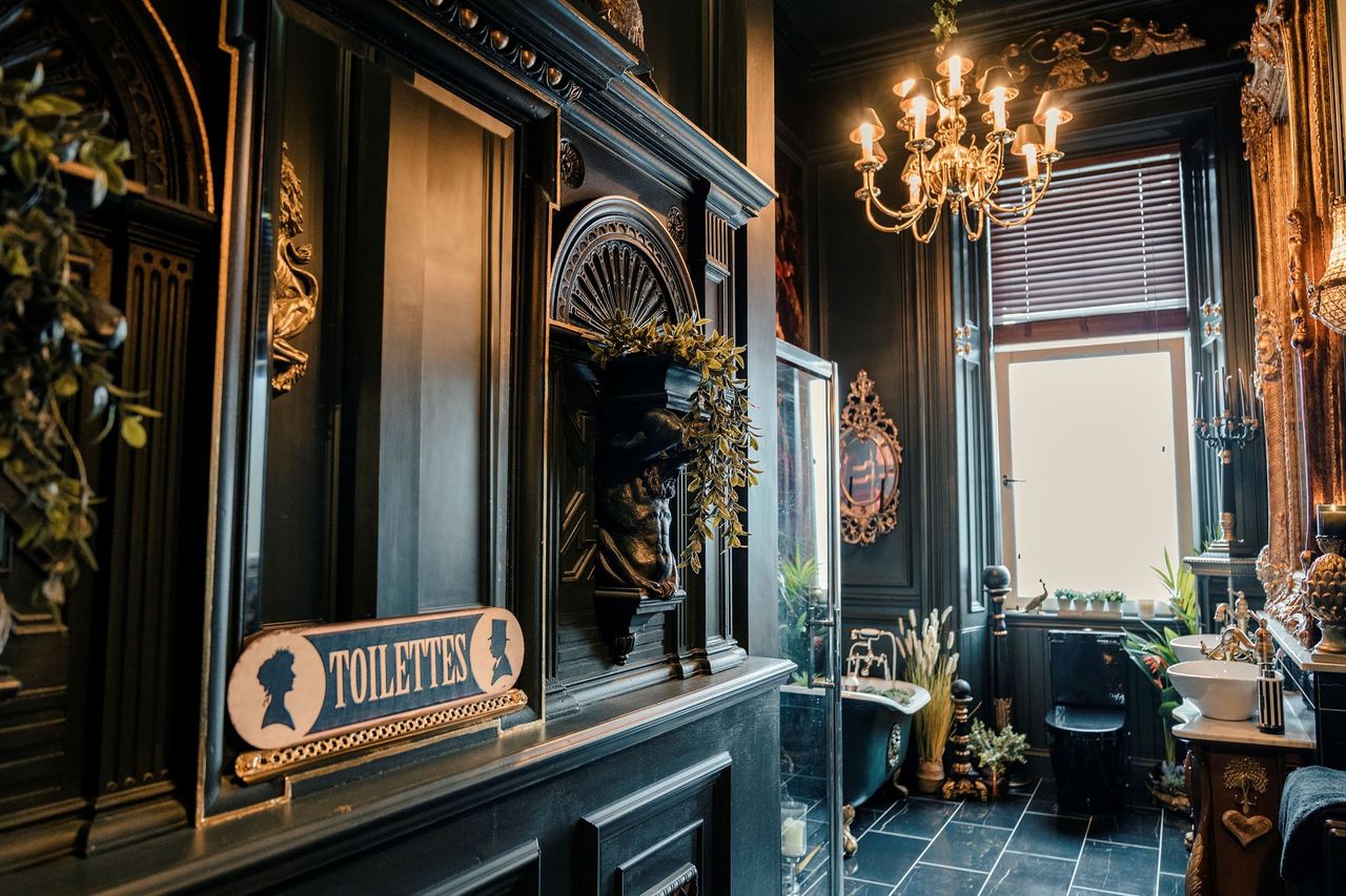 The bathroom has black tiles all round with a black bath and toilet with a paired sinks