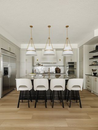 A kitchen with white bar stools, off-white cabinetry, and three pendant shades over a large island