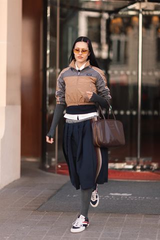 Amelia wears a Miu Miu jacket, bag, skirt, and Gymnasium Sneakers.